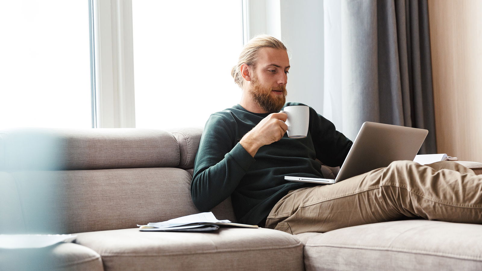 man in green jumper holding mug, completing shamanic training on a laptop